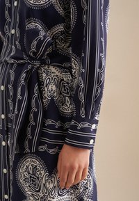 Abito blu navy con motivi paisley bianchi e righe, con vita annodata e polsini con bottoni, realizzato in un tessuto liscio.