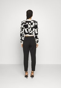 Zwart-witte cropped trui met geometrisch patroon, gecombineerd met zwarte taps toelopende broek en zwarte hakken, met een ontspannen silhouet.