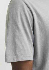 Hellgraues Kurzarm-T-Shirt, aus weichem Material mit einer subtilen Textur. Mit Rundhalsausschnitt und sauber genähtem Saum.