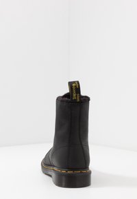 Svart läder ankelboot med fluffigt foder, rund tå, gult stickat detaljer och en dragflik märkt "with soles" bak.