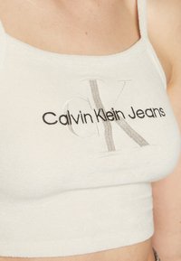 Kraťasy Calvin Klein Jeans, světle krémová látka, hladká textura, zdobené černým a stříbrným vyšívaným logem s nápisem "CK" a "Calvin Klein Jeans".