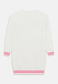 Vit stickad tröja med korta ärmar och rosa ränder vid ärmarnas avslut och nederkant. Enkel, mjuk textur och avslappnad passform.