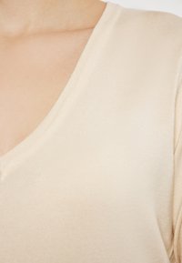 Beige V-hals top met ribbelstructuur, korte mouwen en een getailleerde pasvorm. Zachte stof valt soepel langs de halslijn en schouders.