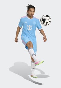 Lyseblå fodboldtrøje med pink detaljer, prydet med et krone-logo. Hvide strømper med sorte striber. Hvide og pink fodboldstøvler. Fodbold i nærheden.
