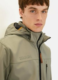 Lichtgrijze softshelljack met een rits aan de voorkant, een verstelbare capuchon en subtiele logodetails. Kenmerkt zich door contrasterende oranje accenten aan de binnenkant.