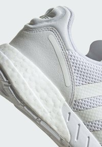 Biele športové topánky s vrchnou časťou z sieťoviny, textúrovaným panelom a polstrovanou podrážkou s ryhovaným vzorom a minimalistickými dizajnovými detailmi.