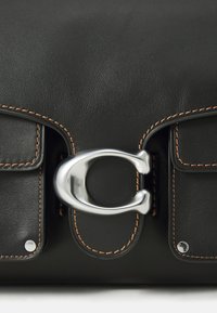 Black leather bag featuring a prominent silver C-shaped clasp, contrasting tan stitching, and two small front pockets.