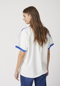 T-shirt bianco con accenti blu sulle maniche, taglio corto e morbido. Abbinato a jeans blu scuro.