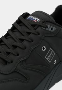 Svart sneaker med teksturert syntetisk overdel, tonale snøring, gummisåle, sølvøyelister og en logopatch med røde og blå detaljer.