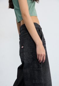 Cargo pants in dark gray denim with multiple pockets, a high waist, and a subtle logo patch on the back. Worn with a mint green crop top.