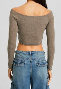 Top marrón de manga larga recortada con diseño de hombros descubiertos combinado con pantalones cargo de mezclilla azul de talle alto, con bolsillos con solapa y corte holgado.