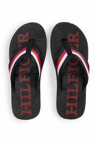 Sorte flip-flops med strukturerede såler, prydet med marineblå, røde og hvide stribede stropper samt ordet "FILL" i rødt på sålen.