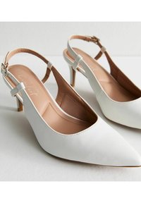 Tacchi slingback bianchi in pelle con punta affusolata e tacco medio affusolato. Fodera interna di un beige chiaro, con una texture liscia e cuciture minime.