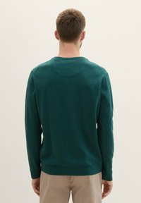 Pulover verde din tricot, cu mâneci lungi, guler rotund și manșete și tiv cu nervuri. Textură netedă, cu variații subtile de nuanță.