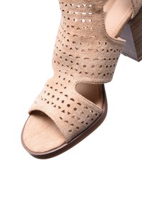 Sandalo in suede beige con tacco, caratterizzato da motivi a intaglio, punta aperta e tacco a blocco con una superficie in legno liscia.