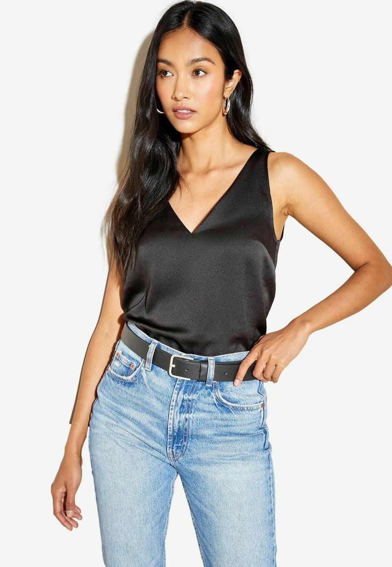 Zwarte satijnen cami met een V-halslijn, gecombineerd met lichtblauwe high-waisted jeans en een zwarte riem, wat een gladde textuur laat zien.