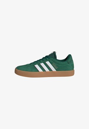 Zapatillas de gamuza verde con tres rayas blancas, suela de goma y diseño bajo. Presentan cierre de cordones y cuello acolchado.