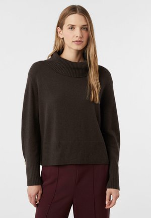 Brązowy, oversize sweter z prążkowanym golfem i mankietami. Miękka tekstura, o prostym kroju i gładkim wykończeniu. Połączony z bordowymi spodniami.
