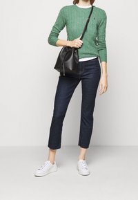 Pull vert en tricot torsadé, jeans courts bleu foncé, baskets blanches et sac seau noir avec cordon de serrage. Éléments de design simples et modernes.