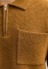 Bruine gebreide pullover met een korte rits bij de nek, ribbelstructuur en een patchzak aan de voorkant. Heeft een klassieke kraagstijl.