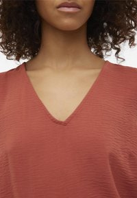 Haut terracotta à col en V avec un tissu texturé et froissé. Coupe ample, manches courtes et encolure lisse, idéal pour une tenue décontractée.
