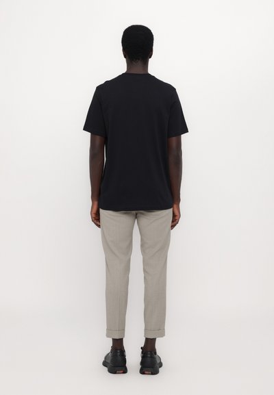 Tricou din bumbac negru cu mâneci scurte, asortat cu pantaloni gri deschis. Pantalonii au mansete răsucite; modelul poartă adidași negri.