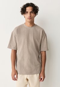 Beige T-shirt met korte mouwen in een zachte, gestructureerde stof met een ronde halslijn en een ontspannen pasvorm. Geen zichtbare patronen of hardwaredetails.