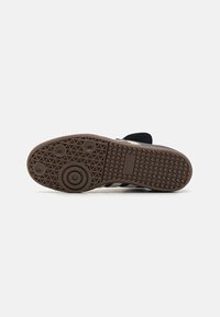 Schuhsohle mit einer gemusterten Gummiunterseite in Braun, die kreisförmige und sechseckige Profilierungen aufweist, sowie ein geprägtes Markenlogo.