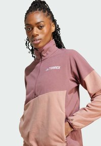 Fleece puuvillapaita puolikorkealla vetoketjulla mauve- ja vaaleanpunaisissa väreissä, jossa on korkea kaulus, kengurupocket ja Terrex-logo valkoisena rinnassa.