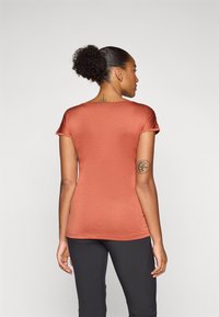 Kortärmad, figurnära t-shirt i en rostorange färg, tillverkad av mjukt, texturerat tyg. Bakdesignen har en rundad halsringning och en böjd nederkant.