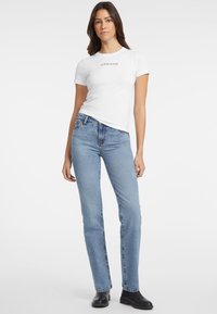 Witte korte mouwen t-shirt met de tekst "GUESS JEANS", gecombineerd met lichtblauwe hoge taille straight-leg jeans en zwarte enkellaarsjes.