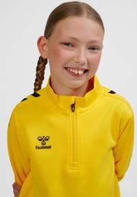 Gul zip-up-jacka i slät tyg. Har svarta detaljer på axlarna och logotypen på vänster bröst. Regular fit, krage design.