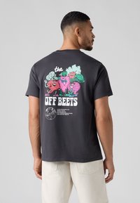 Sötét szürke pamut póló, színes mesefigurás grafikával a hátsó részén, zöldségekkel és a "OFF BEETS" felirattal, rövid ujjakkal és kerek nyakkivágással.