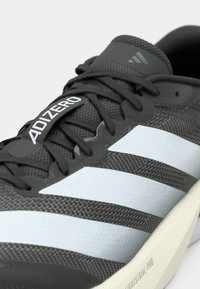 Gros plan d'une chaussure de running Adidas noire et blanche avec des lacets noirs et le mot Adizero sur la languette.