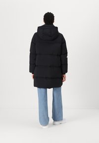 Black puffer jacket with a hood and horizontal quilted design. Features a relaxed fit, long sleeves, and slightly rounded hem. Paired with light blue wide-leg jeans and white shoes.