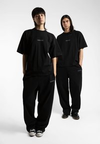 Schwarze, übergroße T-Shirts mit kurzen Ärmeln und kleinem Logo auf der Brust, kombiniert mit passenden schwarzen Sweatpants; beide aus weichem Stoff gefertigt.