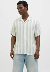 Chemise à manches courtes à boutons en tissu léger avec des rayures verticales vertes et blanches. Dotée d'un col et d'une coupe décontractée, associée à un denim clair.