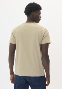 Tricou bej cu mâneci scurte, realizat dintr-un material moale, cu guler la baza gâtului și o croială lejeră, asortat cu blugi din denim de culoare bleu închis.