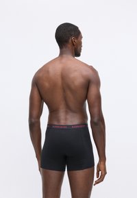 Fekete boxer alsónadrág piros "BJÖRN BORG" derékkal, egy férfi modellen látható, hátulról nézve, sima, feszes kialakítással.