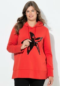 Sudadera roja con un diseño de estrella negra de lentejuelas en el frontal, mangas largas, capucha ajustable y un corte relajado. Textura suave y dobladillo recto.