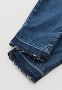 Jambes de jean denim bleu avec des ourlets effilochés et usés, montrant des coutures visibles et un léger délavage du tissu.