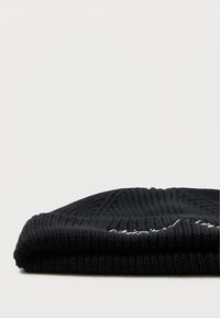 Sort ribbede strikkede beanie foldet med delvist synlig hvid broderet tekst på en ensfarvet hvid baggrund.