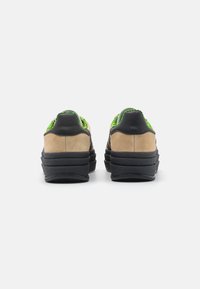 Black and beige sneakers with a textured suede finish, featuring green accents and layered sole design. Rear view shows a low-top silhouette.