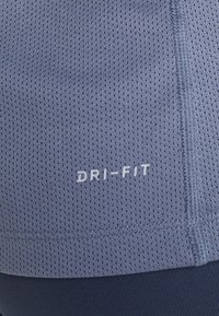 Šedé tričko z síťoviny s bílým logem "DRI-FIT", vybavené malými perforacemi a detailním prošitým švem.