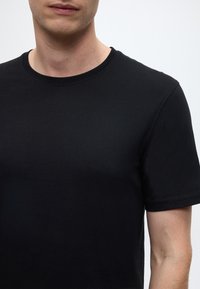 Schwarzes Baumwoll-T-Shirt mit Rundhalsausschnitt, kurzen Ärmeln, glatter Textur und minimalistischem Design, das eine Nahaufnahme des Oberkörpers zeigt.