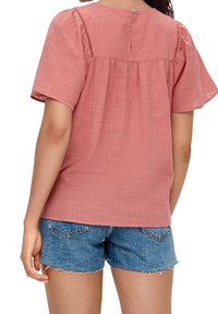 Blush-pink Kurzarmtop aus strukturiertem Stoff mit Knopfverschluss hinten und gerafften Details, kombiniert mit blauen Jeansshorts.
