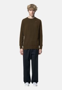 Maglione marrone lavorato a maglia con polsini e orlo a coste, abbinato a pantaloni larghi blu navy e sneakers bianche. Design semplice, senza motivi.