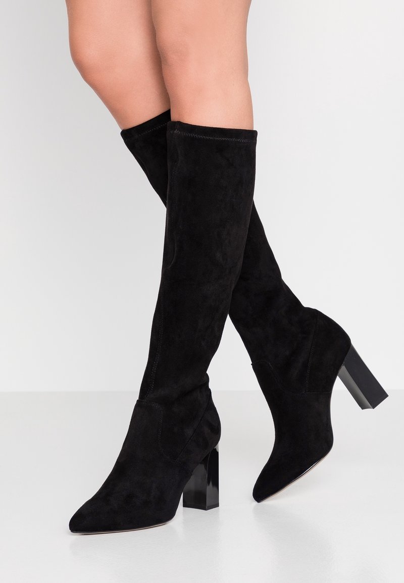 Bottes montantes en daim noir avec bout pointu et talon bloc épais. Texture lisse avec un minimum de coutures pour une apparence élégante.