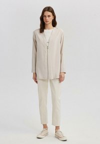 Lysbeige oversized jakke med en tekstureret overflade, lynlåslukning foran og lange ærmer, parret med matchende cremefarvede tapered bukser og sneakers.