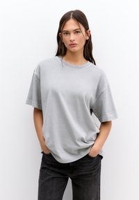 T-shirt gris à manches courtes avec une coupe décontractée, un col rond et une texture douce, associé à un jean noir. Aucun motif ou élément visible.